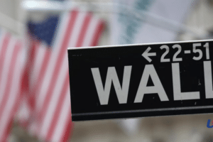 Close-up of a Wall Street street sign with blurred U.S. flags in the background.