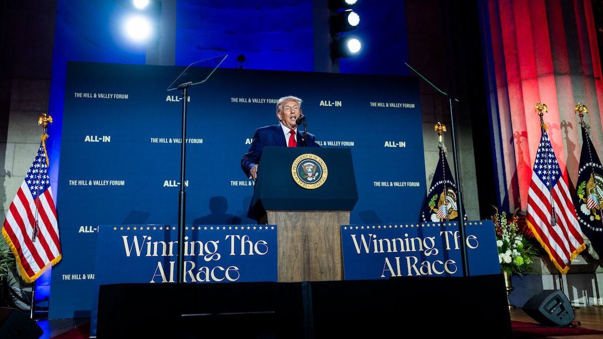 Donald Trump speaks behind a podium at the White House AI Summit, flanked by “Winning the AI Race” signs.