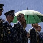 Pete Hegseth stands alongside military officials in the rain during a Pentagon ceremony.