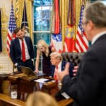 Donald Trump and Natalie Harp review a laptop in the Oval Office as JD Vance looks on.