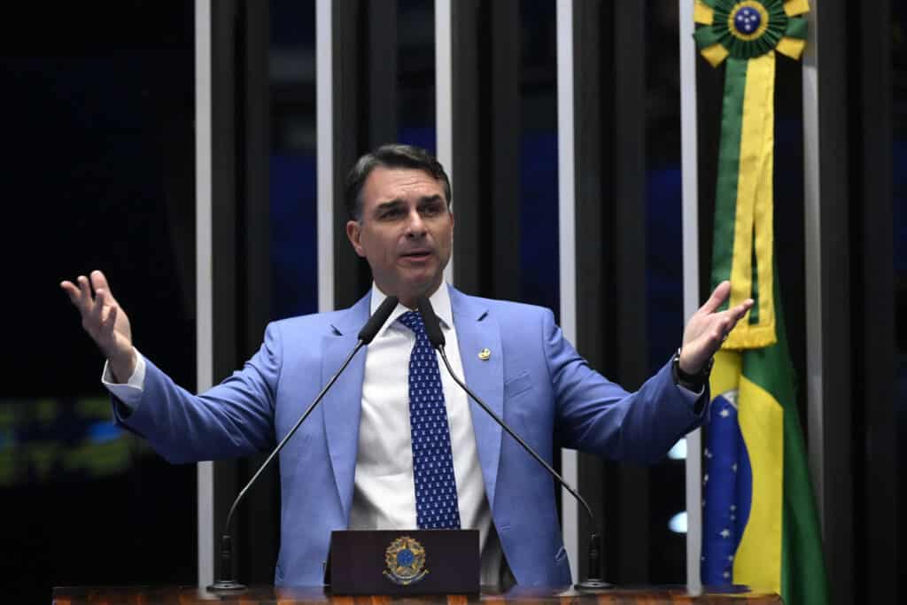 Flávio Bolsonaro speaks at Brazil’s Senate in Brasília, gesturing with both hands beside a Brazilian flag.