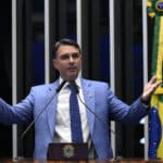 Flávio Bolsonaro speaks at Brazil’s Senate in Brasília, gesturing with both hands beside a Brazilian flag.