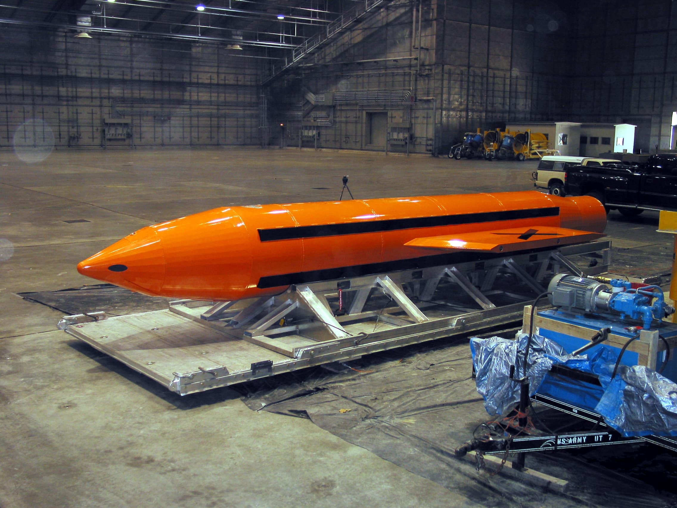 Orange GBU-43/B MOAB, nicknamed the mother of all bombs, resting on a transport platform inside a hangar.