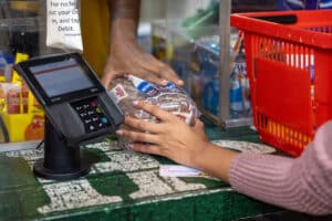 Shopper places a loaf of bread beside a payment terminal at a grocery checkout.